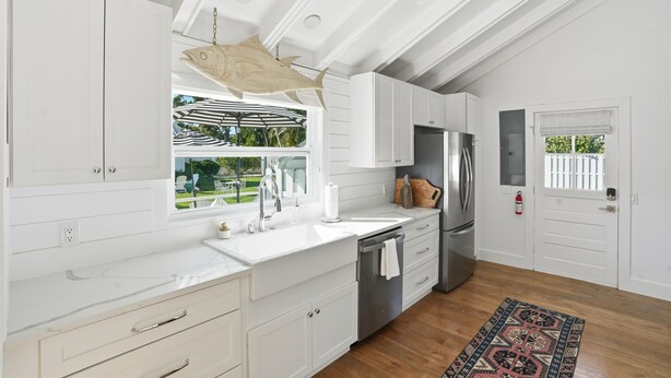 Una cocina moderna con armarios blancos, una isla grande, electrodomésticos de acero inoxidable y vistas al exterior.