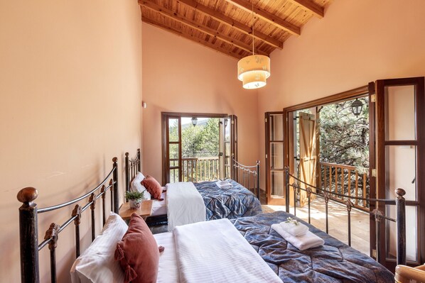 Un dormitorio con dos camas, techo de madera y un balcón con vistas a árboles.