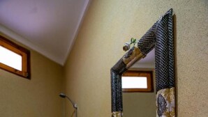 Un bany amb taulell de marbre, un plat decoratiu, un mirall amb emmarcament estampat i una zona de dutxa.