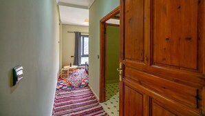 Un passadís amb una porta de fusta, una catifes de ratlles de colors i una taula petita amb una ampolla.