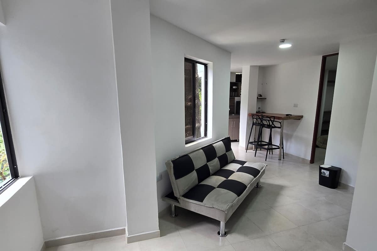 A modern living room with a sofa, a dining table with chairs, and a kitchen area in the background.