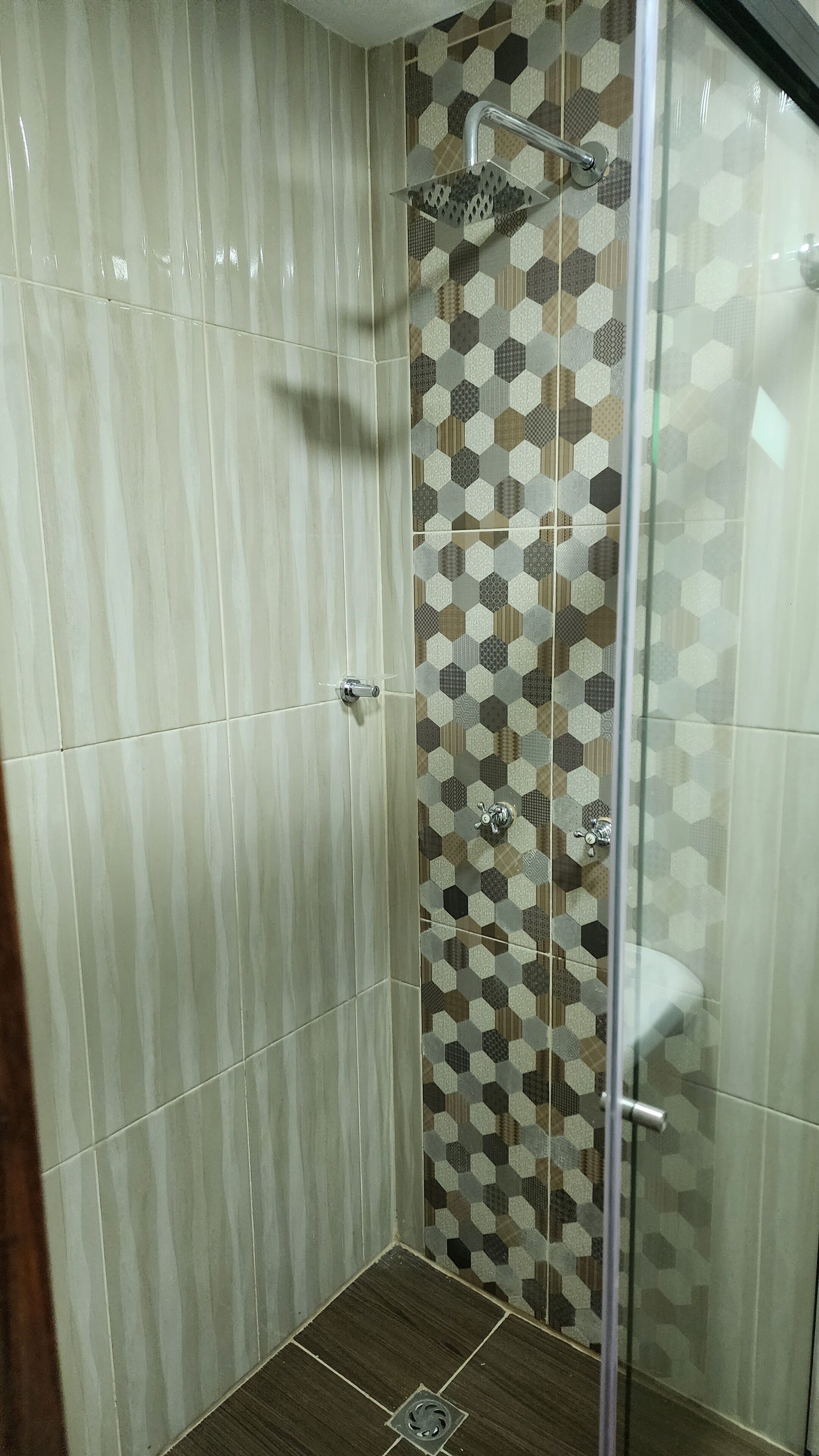 A shower with a glass door, tiled walls, and a hexagonal pattern.