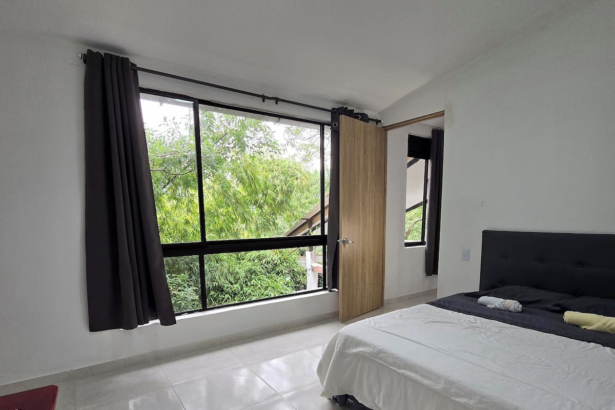 A bedroom with a large window, a bed, a bedside table, and a wardrobe.