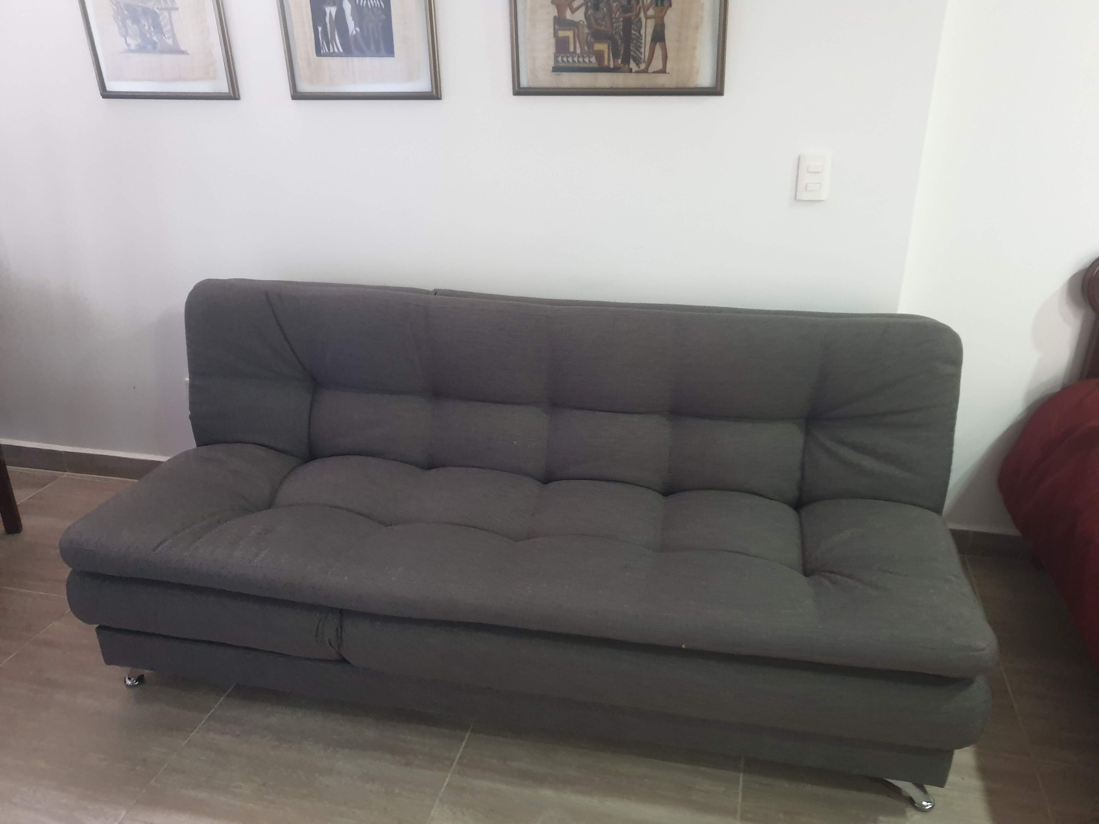 Un sofá gris en una habitación con suelo de baldosas y pared blanca.