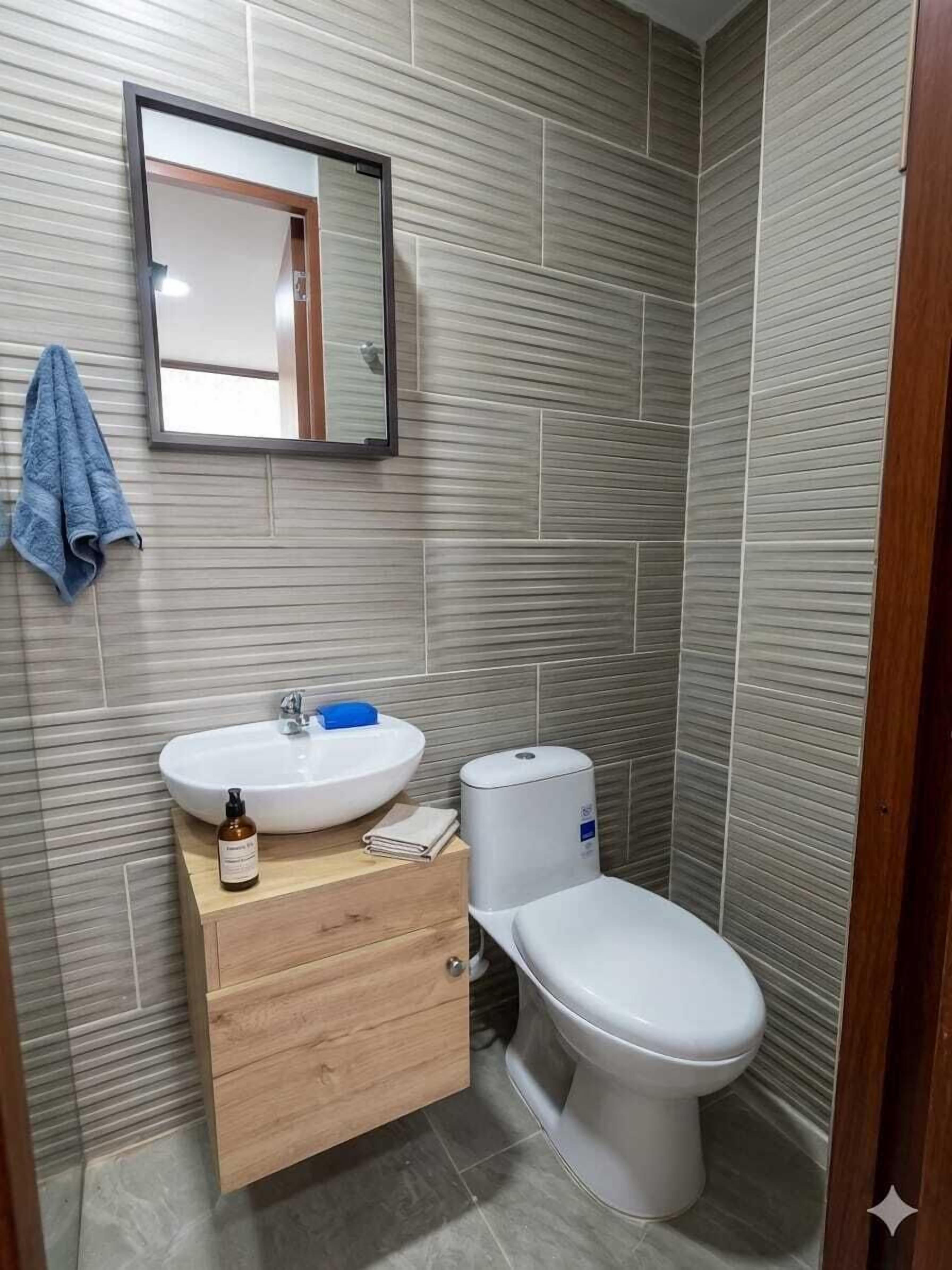 A bathroom with a wooden vanity, a white sink, a mirror, and a toilet.