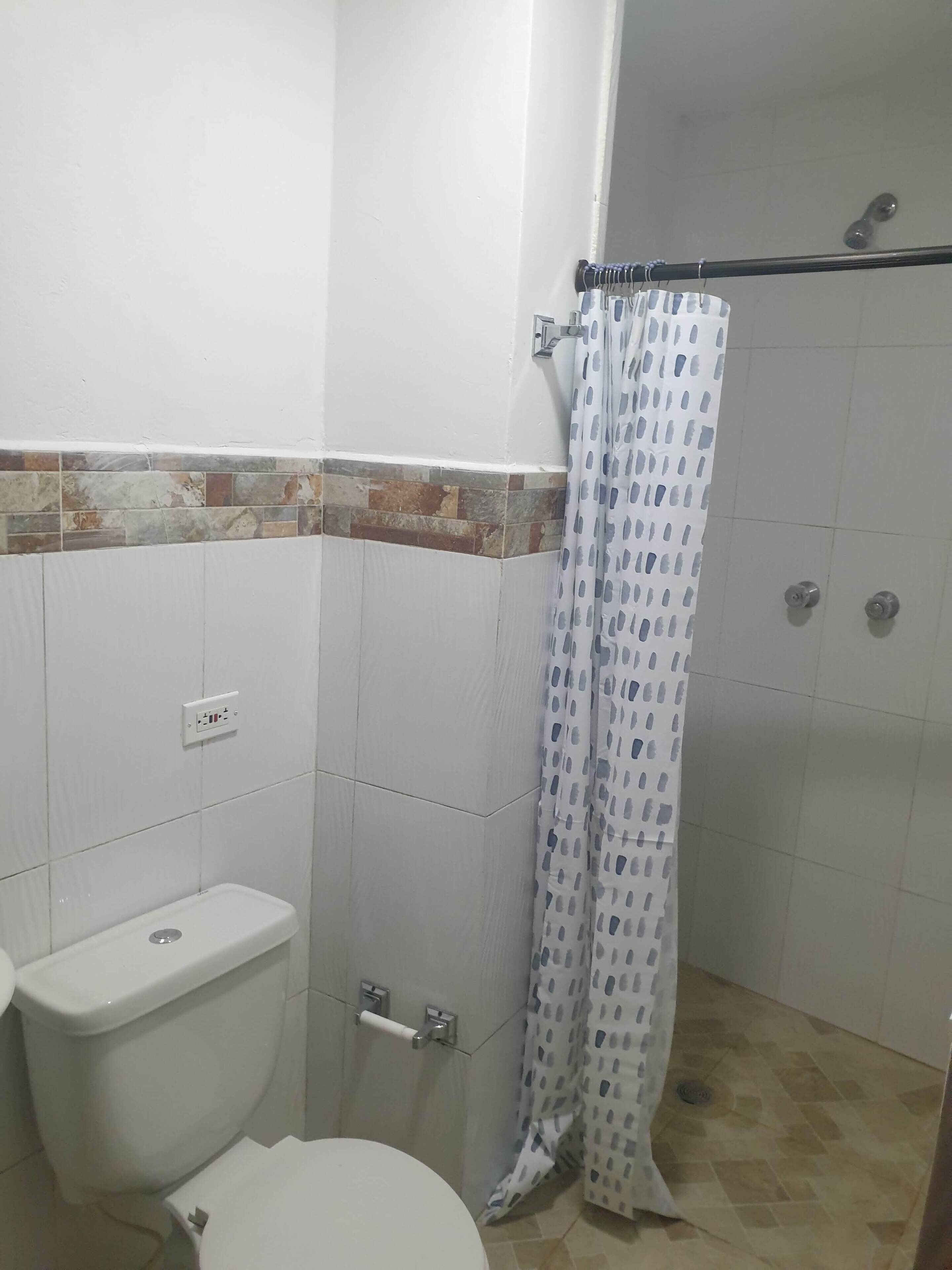 A bathroom with a toilet, a shower with a curtain, and a tiled floor.