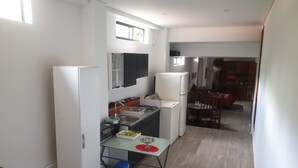 A compact kitchen with white appliances, a dining area with a table and chairs, and a staircase leading to another level. - PILARICA GARDENS (Medellín)