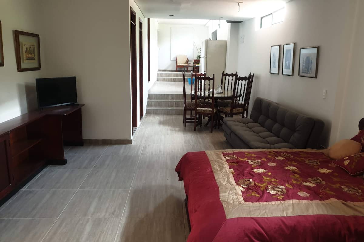 A hotel room with a bed, a TV, a sofa, and a dining area with chairs and a table.