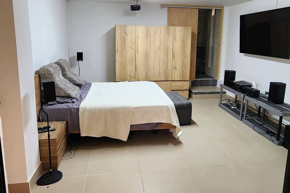A bedroom with a bed, a wooden wardrobe, a television, and a speaker system.