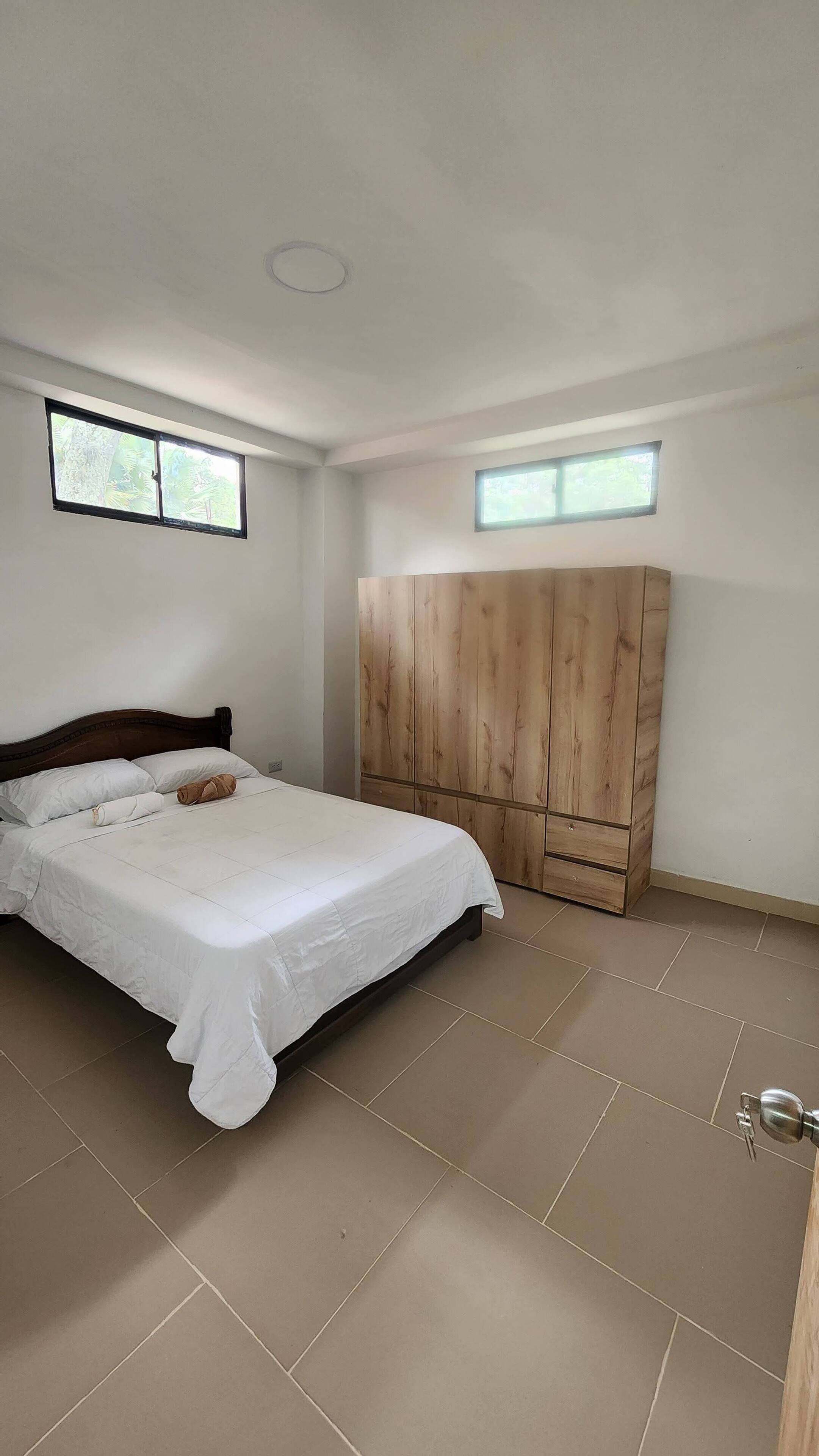 Quarto com cama, guarda-roupa de madeira e janela.