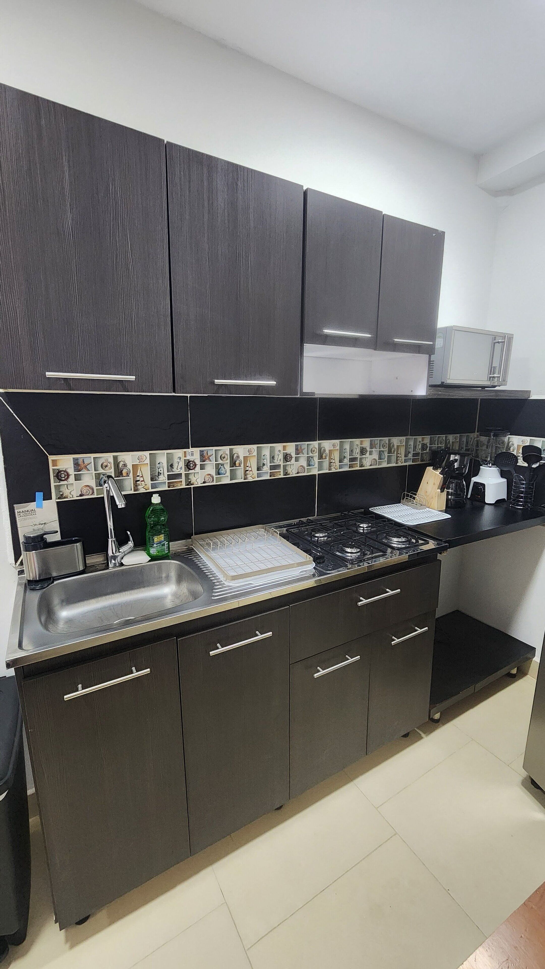 A modern kitchen with dark cabinets, a stainless steel sink, and a tiled backsplash.