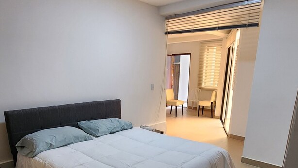 A bedroom with a bed, a chair, a crib, and a bathroom visible in the background. - PILARICA GARDENS (Medellín)