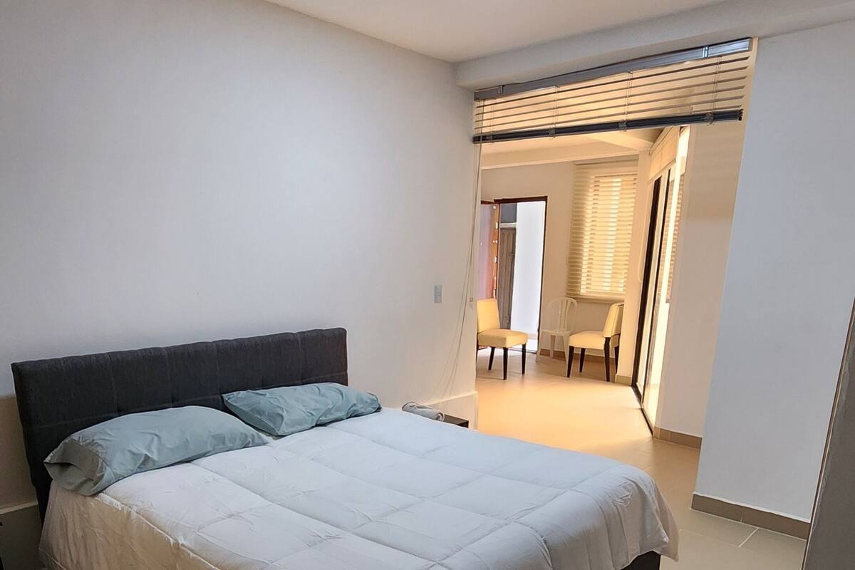 A bedroom with a bed, a chair, a crib, and a bathroom visible in the background.