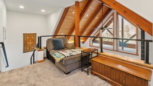 Une chambre confortable située sous les toits, avec un plafond en pente, un banc en bois, un canapé et une grande fenêtre donnant sur l’extérieur.