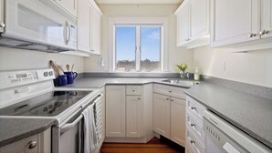 A modern kitchen with white cabinets, a double sink, and a window with a city view. - Sunshine & Seascapes, Biddeford Pool (Biddeford)