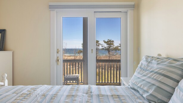 A bedroom with a bed, a view of the beach through a sliding door, and a small wooden bench outside. - Sunshine & Seascapes, Biddeford Pool (Biddeford)