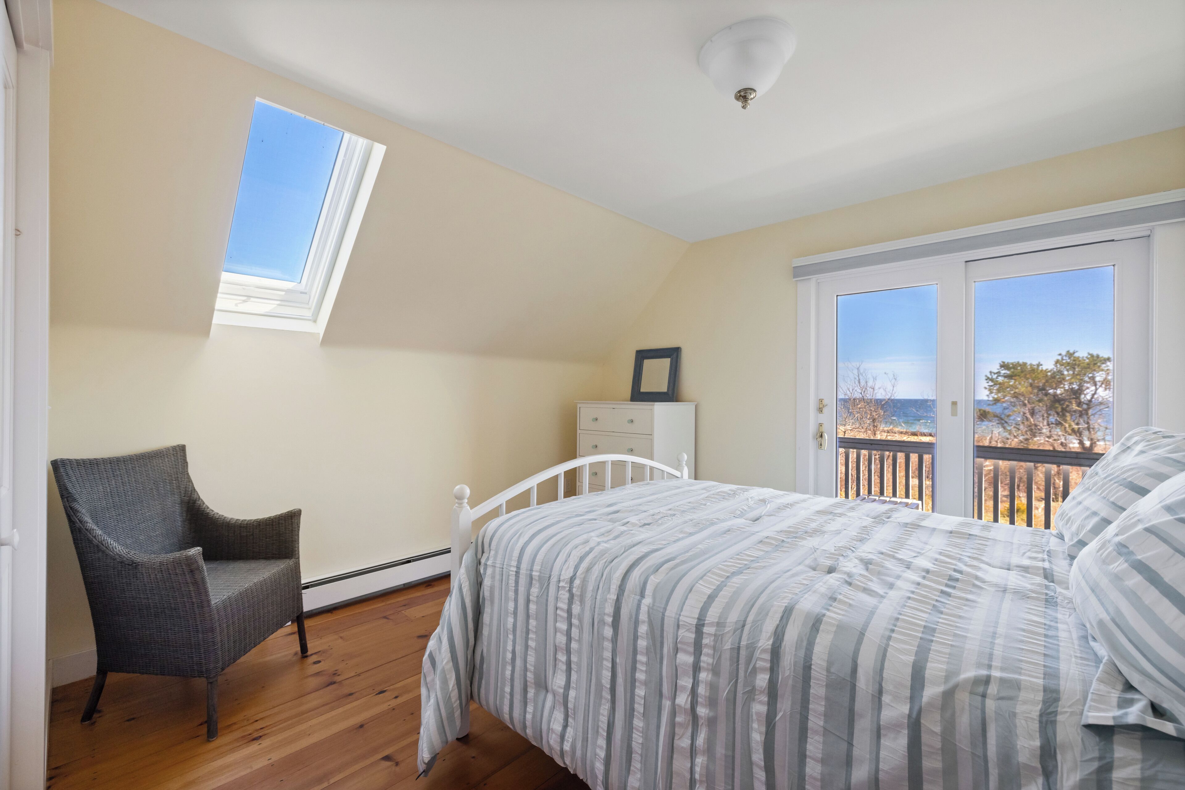 A bedroom with a bed, a chair, a dresser, and a window overlooking a balcony.