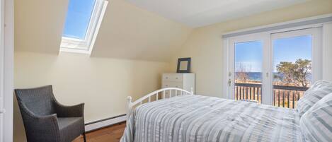 A bedroom with a bed, a chair, a dresser, and a window overlooking a balcony.