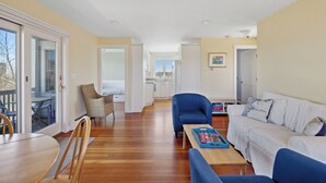 A spacious living area with a wooden floor, a white sofa, a blue armchair, and a dining table with chairs. - Sunshine & Seascapes, Biddeford Pool (Biddeford)