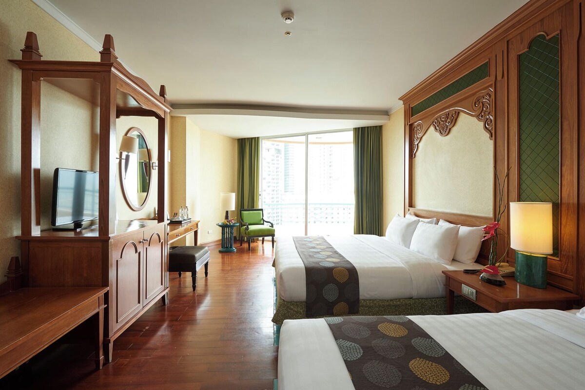 Une chambre d’hôtel avec deux lits, un bureau, une chaise, une télévision et une grande fenêtre avec des rideaux.