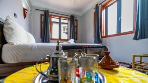A room with a bed, a table with glasses and a teapot, and a view of the outside through a window.