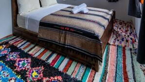 A bedroom with a bed, a colorful rug, a decorative ceiling light, and a window with curtains.