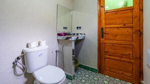 A small bathroom with a toilet, a sink with a mirror, and a wooden door with a frosted glass panel.