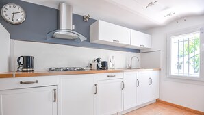 Uma cozinha moderna com armários brancos, coifa de aço inoxidável e janela com vista para o verde.