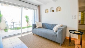 Uma sala de estar moderna com um sofá cinzento, uma mesinha preta e uma porta de vidro que dá para um pátio.