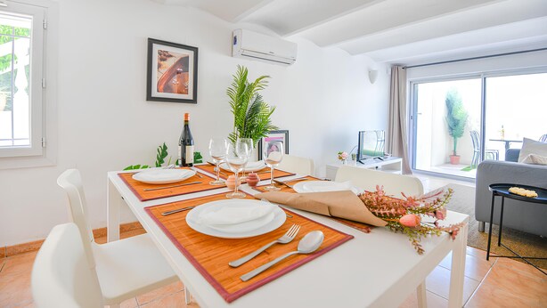 Uma sala de jantar com uma mesa posta para quatro pessoas, uma planta em vaso e um quadro na parede.