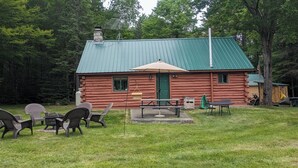 Une cabane en rondins avec un toit en métal vert, une porte verte et un petit espace de véranda doté de sièges d’extérieur.