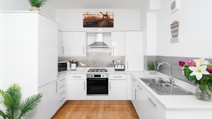 A modern kitchen with white cabinets, a stainless steel range hood, a microwave, a toaster, and a sink with a faucet. - 3 bedroom accommodation in Woolacombe (Woolacombe)