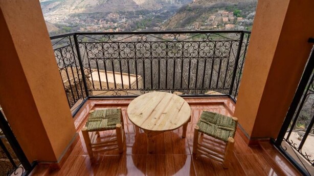 Een balkon met een houten tafel en twee stoelen, met uitzicht op een bergachtig landschap.