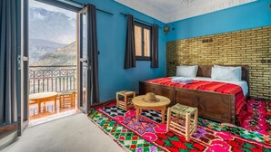 Een kamer met een groot bed, een balkon met uitzicht op bergen en een kleurrijk vloerkleed.