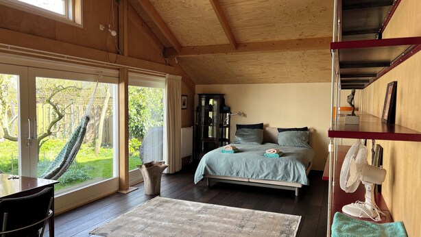 A bedroom with a bed, a desk, a chair, a window, and a view of the outdoors.