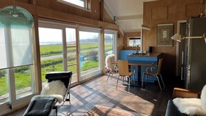 A spacious room with large windows, a kitchen area, and a cozy seating area with a fur-covered chair.
