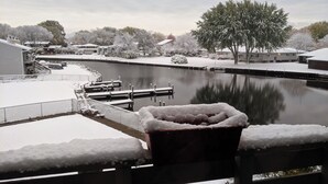 A snow-covered outdoor area with a dock extending into a body of water, surrounded by trees and buildings. - Lake Channel 'Brewhaus' Townhouse: 2 bedrooms with 6 levels on Lake Winnebago (Oshkosh)