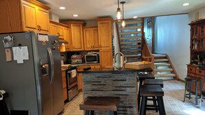 A kitchen with wooden cabinets, a granite island, a stainless steel refrigerator, a microwave, and a staircase leading to a loft. - Lake Channel 'Brewhaus' Townhouse: 2 bedrooms with 6 levels on Lake Winnebago (Oshkosh)