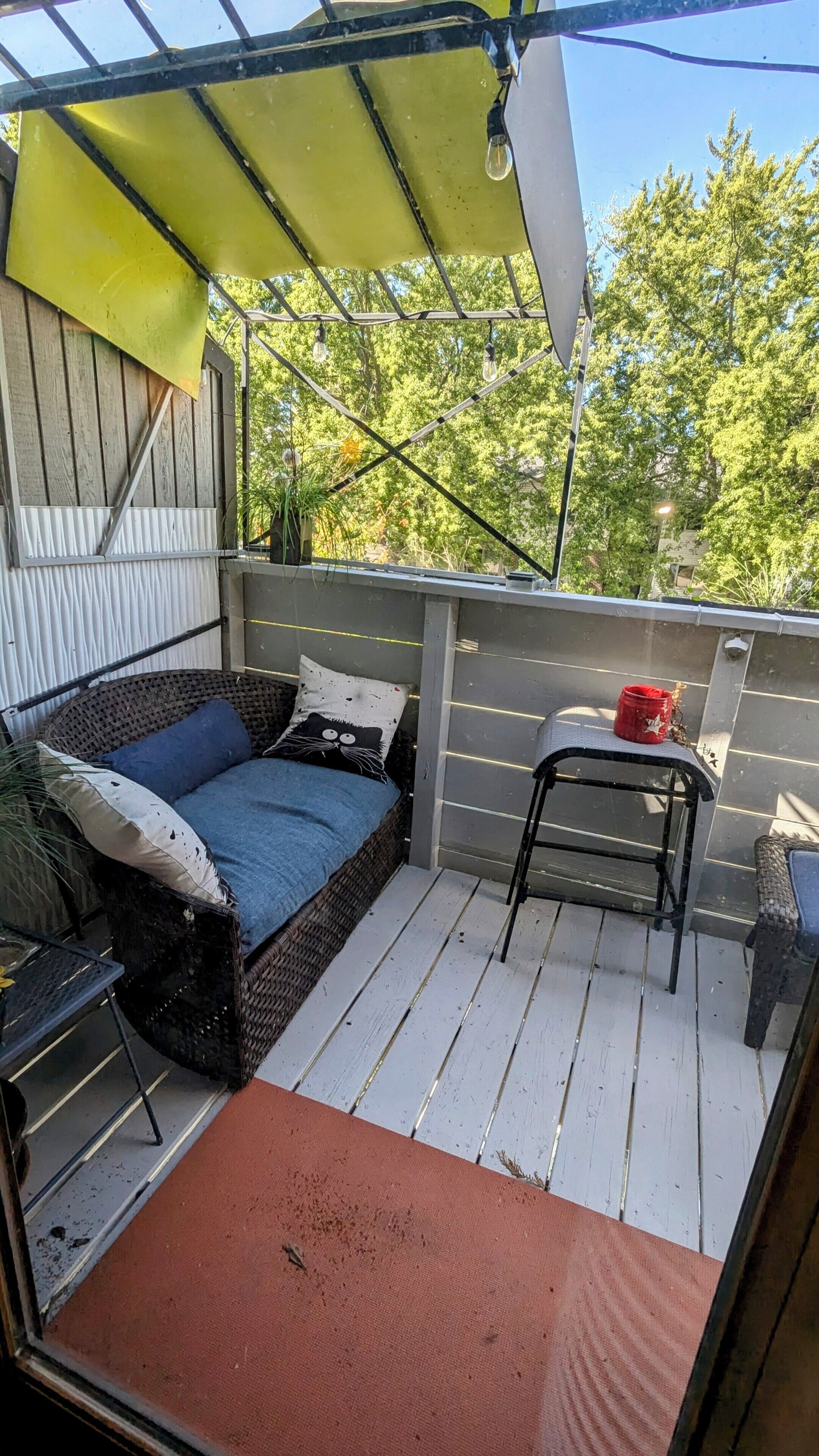 A small outdoor patio with a wicker sofa, a red bucket, and a metal chair.