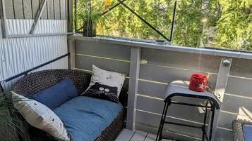 A small outdoor patio with a wicker sofa, a red bucket, and a metal chair.
