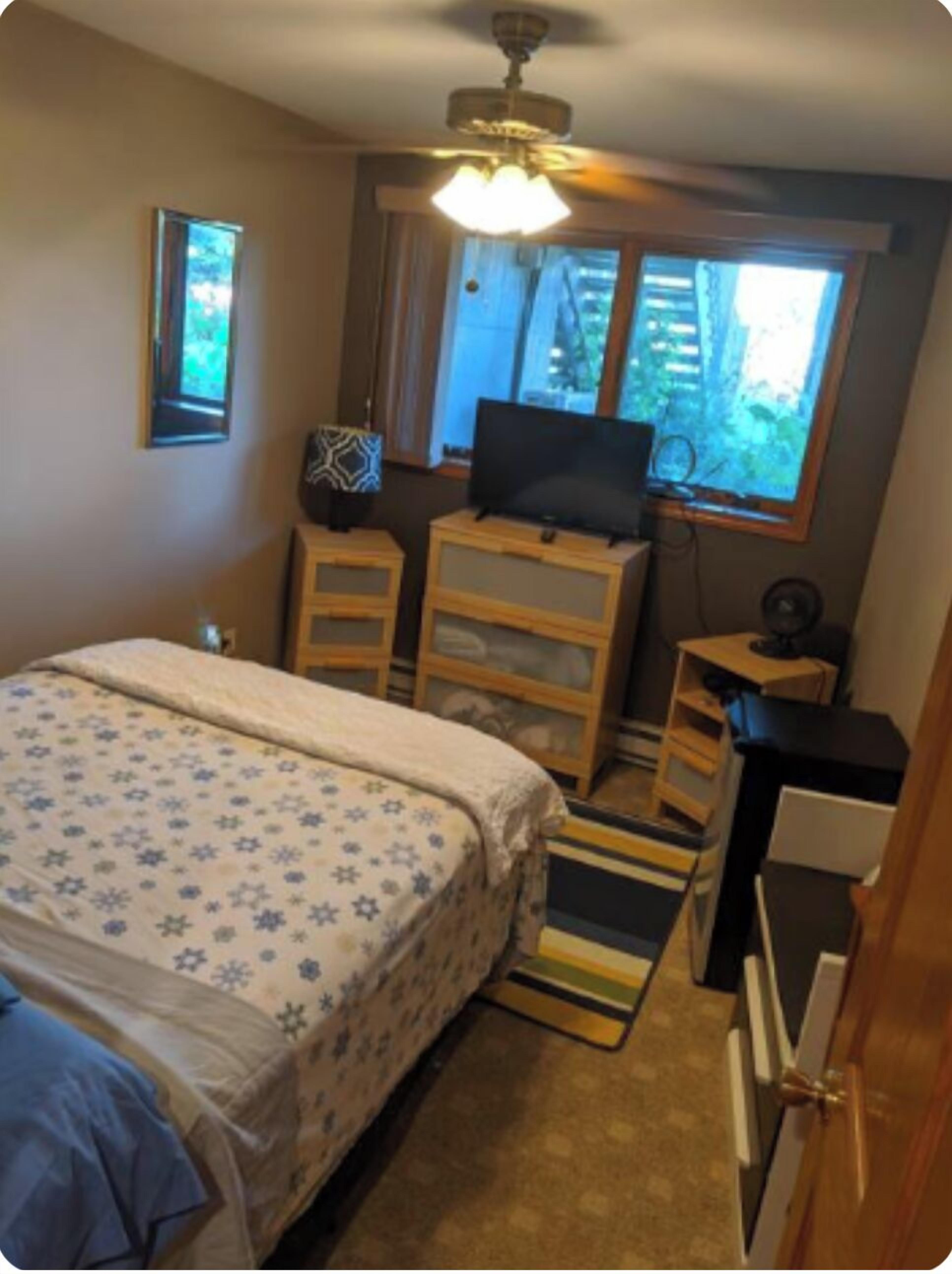 A bedroom with a bed, a desk, a television, and a window.
