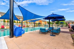 Un espace piscine agrémenté de parasols bleus, de chaises longues et d’une piscine.