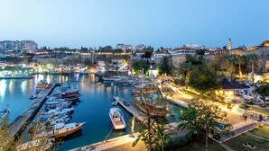 A marina with boats docked, a stone fort, and buildings along the waterfront. - Perge Pine Green (Antalya)