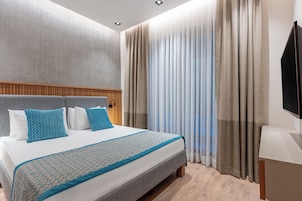 Una habitación de hotel moderna con una cama grande, cabecero de madera y un televisor a la derecha.
