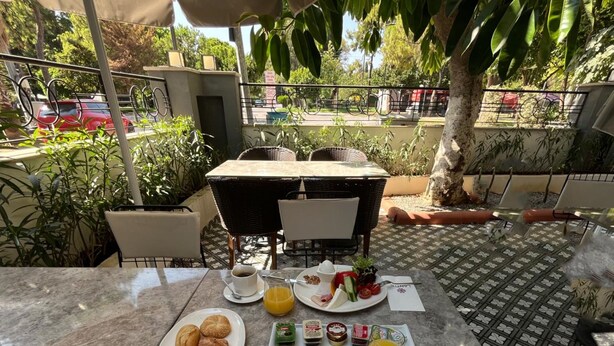 An outdoor dining area with a table set for breakfast, including plates of food, drinks, and a menu. - Perge Pine Green (Antalya)