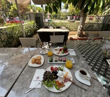 Un área de comedor al aire libre con una mesa dispuesta para el desayuno, incluyendo platos de comida, bebidas y un menú.