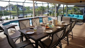 A dining area with a view of a lake, a pool, and a blue outdoor sofa. - Cozy Retreat, pool, fresh water canal, bbq grill , fire pit, electric bikes. (Cape Coral)