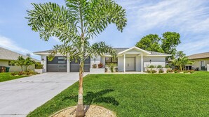 A modern two-story house with a well-maintained lawn and a single tree in the front yard. - Cozy Retreat, pool, fresh water canal, bbq grill , fire pit, electric bikes. (Cape Coral)