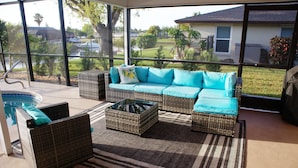A covered outdoor seating area with wicker furniture and a view of a residential neighborhood. - Cozy Retreat, pool, fresh water canal, bbq grill , fire pit, electric bikes. (Cape Coral)
