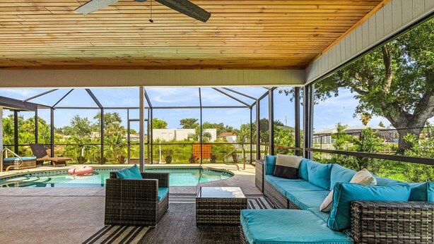 A covered outdoor area with a pool, wicker furniture, and a view of the surrounding greenery. - Cozy Retreat, pool, fresh water canal, bbq grill , fire pit, electric bikes. (Cape Coral)